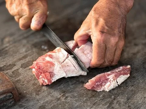 Hands skillfully cutting raw meat on wooden surface for culinary preparation Stock Photos