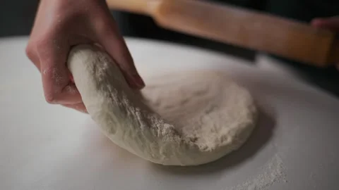 Hands skillfully flatten dough with wooden roller on clean countertop Stock Footage 336095900