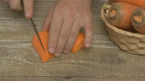 Hands Skillfully Preparing Fresh Carrots on a Rustic Wooden Table for a Stock Footage 282581898