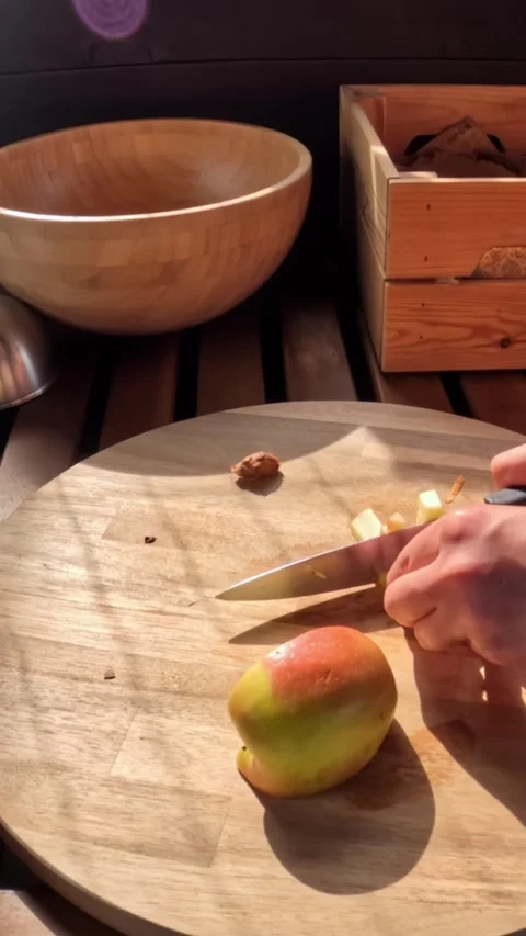 Hands slice an apple on a wooden board in warm sunlight, preparing fresh Stock Footage 323338758
