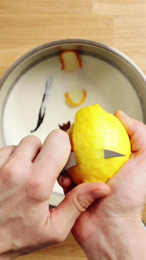 Hands slice lemon peel and drop it into milk mixture. Stock Footage 345273443
