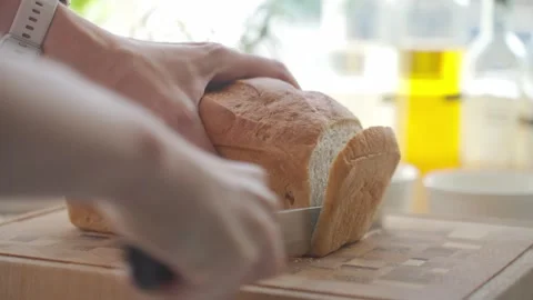 Hands slice loaf of bread on cutting board in kitchen Stock Footage 339963447