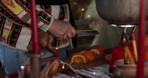 Hands slice orange fruit on wooden cutting board with blurry Christmas lights Video stock 165386328