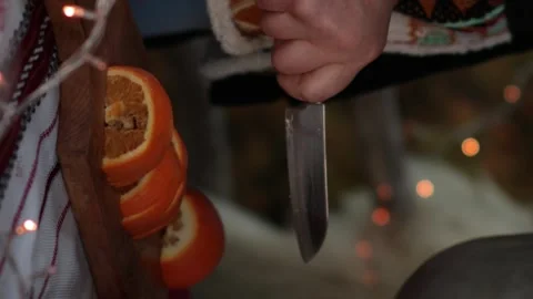 Hands slice orange fruit on wooden cutting board with blurry Christmas lights Video stock 166364761