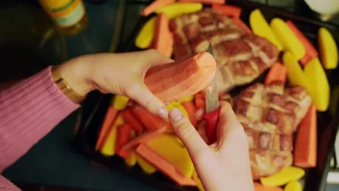 Hands slice sweet potato rounds over a sheet pan with crosshatched pork and Stock Footage 328951161