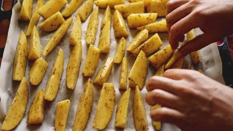 Hands - Sliced raw potatoes on a baking sheet with spices and rosemary, top view Stock Photos