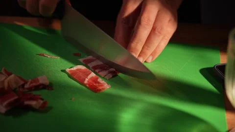 Hands slicing bacon strips on green cutting board in kitchen Stock Footage 312343861