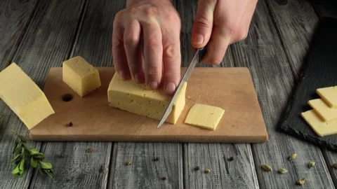 Hands slicing cheese block into smaller pieces on wooden cutting board with Stock Footage 337585919