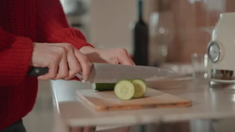 Hands slicing cucumber into stacked round slices on wooden cutting board in home Stock Footage 346642424