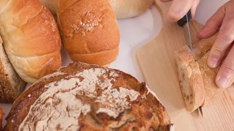Hands Slicing Fresh Bread on Wooden Board with Bakery Assortment Stock Footage 338041684