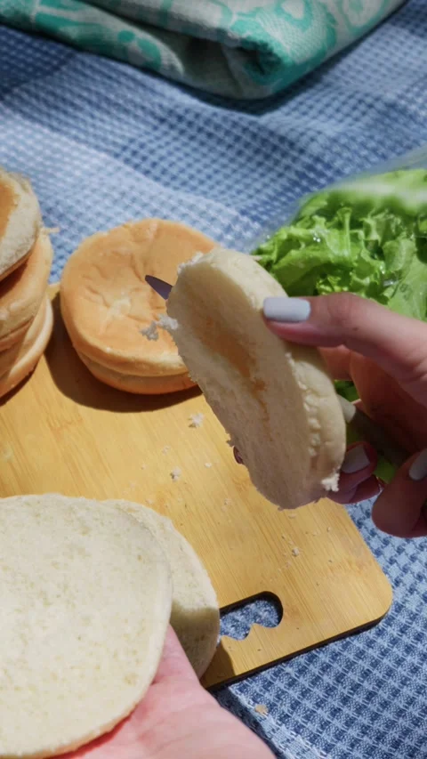Hands Slicing Fresh Hamburger Buns on Cutting Board at Outdoor Picnic Stock Footage 342000536