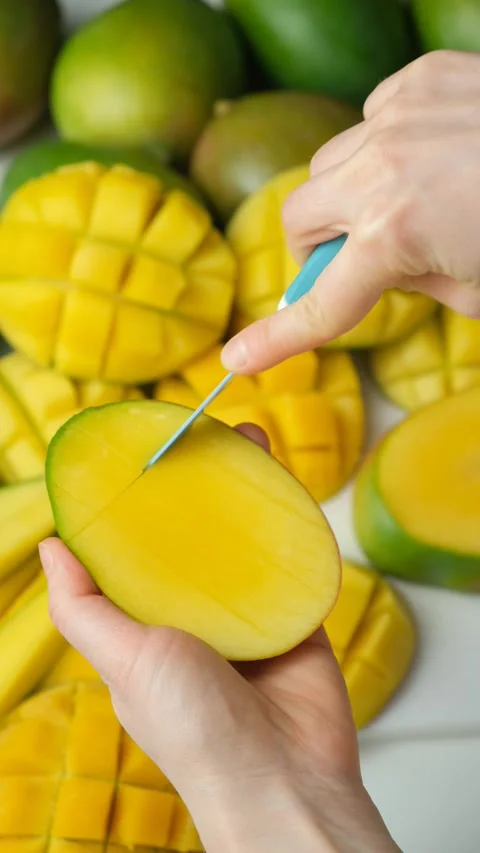 Hands slicing fresh mango with a knife into cubes for hedgehog cut Stock Footage 325888102