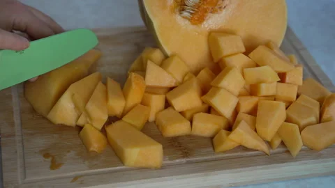 Hands slicing fresh orange pumpkin on wooden cutting board Vídeo Stock 338121027