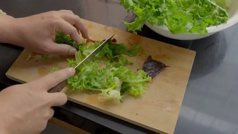 Hands slicing fresh organic leafy greens on wooden board in kitchen Stockbeeldmateriaal 338144524