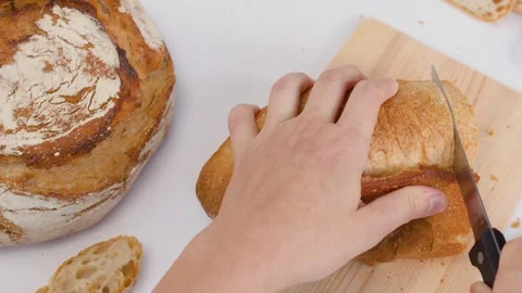 Hands Slicing Fresh Sourdough Bread on Wooden Cutting Board Stock Footage 337394895