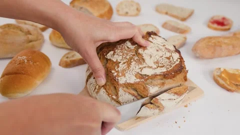 Hands Slicing Fresh Sourdough Bread on Wooden Cutting Board Stock Footage 337518960