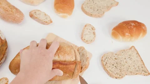 Hands Slicing Fresh Sourdough Bread on Wooden Board with White Background Stock Footage 337533280