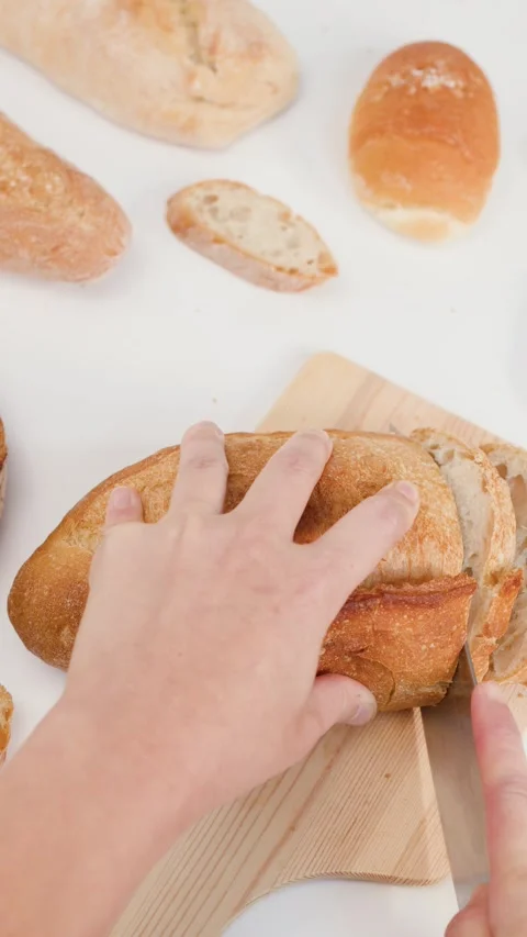 Hands Slicing Fresh Sourdough Bread on Wooden Board with Knife Stock Footage 337535583
