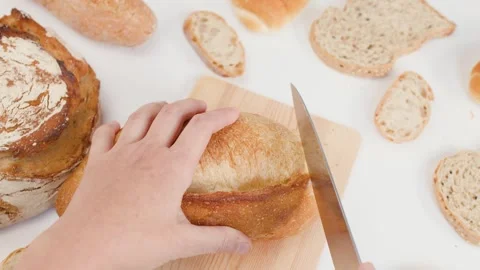 Hands Slicing Fresh Sourdough Bread on Wooden Board with White Background Stock Footage 337746759
