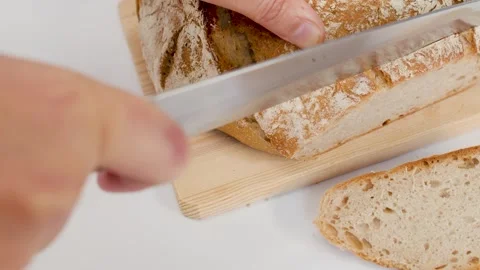 Hands Slicing Fresh Sourdough Bread Loaf on Wooden Cutting Board Stock Footage 337876811