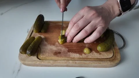 Hands slicing green pickled cucumbers with a kitchen knife on a wooden chopping Stock Footage 335598333