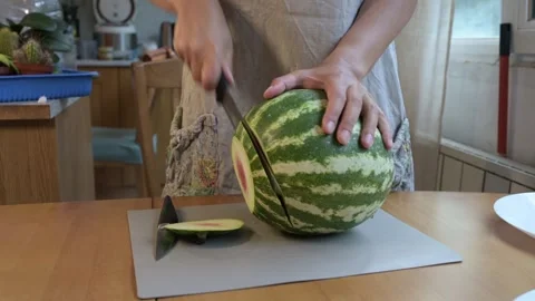 Hands slicing a large striped watermelon on a cutting board in a home kitchen Stock Footage 318242091