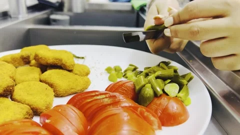 Hands slicing pickled cucumber onto plate with nuggets, close up shot Stock Footage 345166305