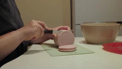 Hands slicing pink sausage into even circular discs Stock Footage 342362081