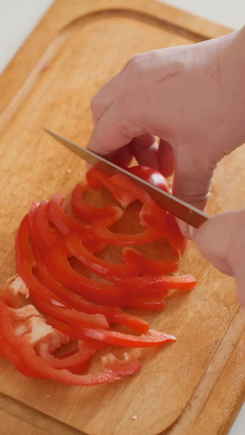 Hands slicing ripe red tomato into thin rings on wooden cutting board, knife Stock Footage 345658245