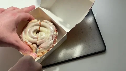 Hands slicing sweet cinnamon roll bun with cream glaze using knife Vídeo Stock 343981473