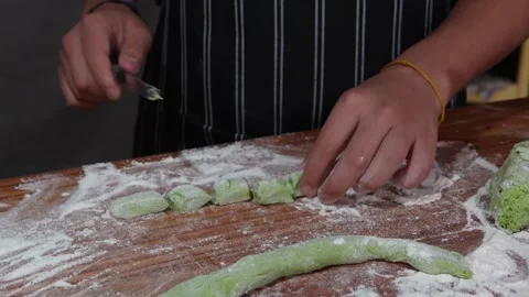 Hands slicing vibrant green gnocchi dough on a wooden board 库存影片 314092760