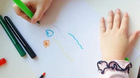 Hands of a small child. child draws flowers with a green pencil on white paper. Stock Footage 128218970