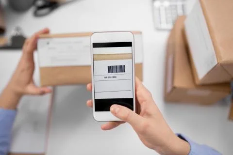 Hands with smartphone scans barcode on parcel box Stock Photos