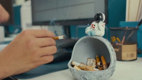 Hands Smoking Cigarettes at Office Desk with Astronaut Figurine Stock Footage 336545340