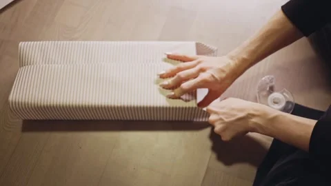 Hands Smooth and Tape Striped Wrapping Paper Neatly Around a Christmas Gift - Stock Footage 332684375