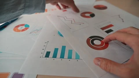 Hands sort through various printed red charts and graphs showing data trends and Stock-Footage 338302589