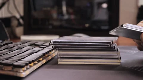 Hands sorting CD cases beside a vintage keyboard on desk, organizing physical Stock-Footage 312371131