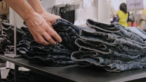 Hands sorting through stack of folded fashionable jeans. Person is looking for Stock Footage 255888721