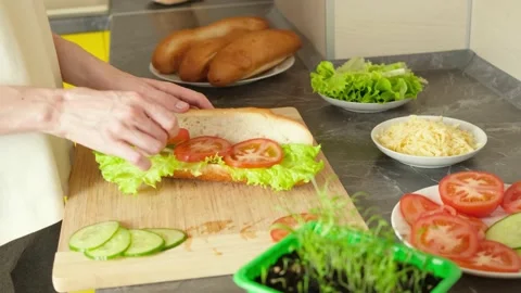 Hands spread tomatoes and cucumbers on a sandwich bun Stock Footage 152094240