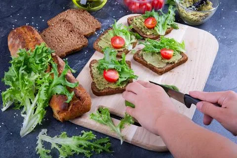 Hands spreading cream on fresh bread with vegetables Stock Photos