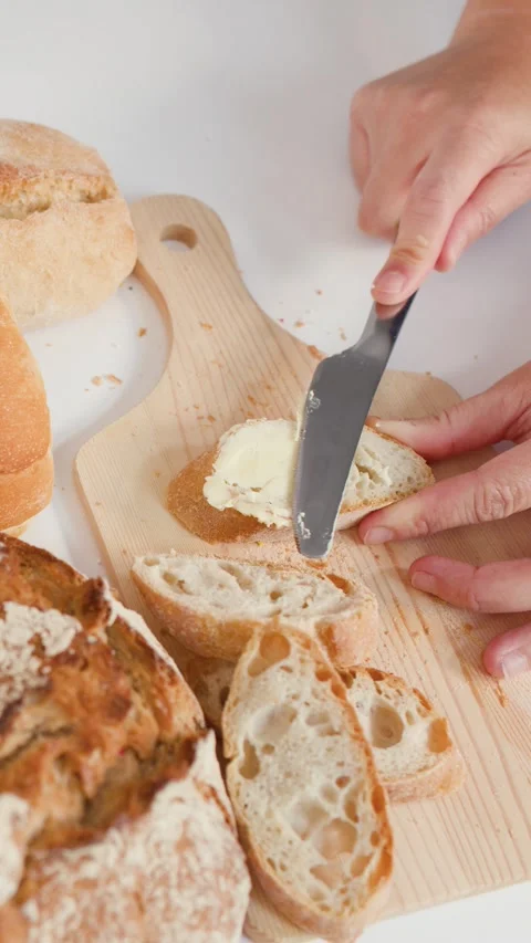 Hands Spreading Fresh Butter on Sliced Artisan Baguette Bread Stock Footage 337519933