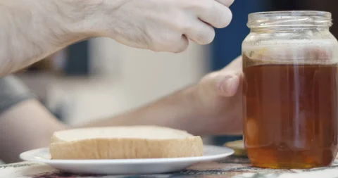 Hands spreading honey on a slice of bread for breakfast - slow motion Stock Footage 147339116