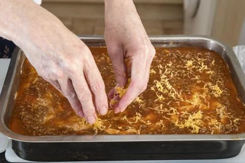Hands sprinkle cheese over savory baked dish Stock Photos