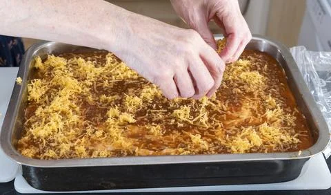 Hands sprinkle cheese over savory casserole dish Stock Photos