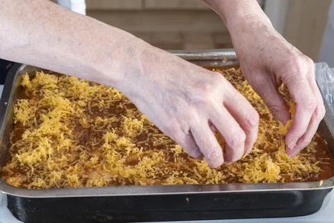 Hands sprinkle shredded cheese over a baking dish Stock Photos