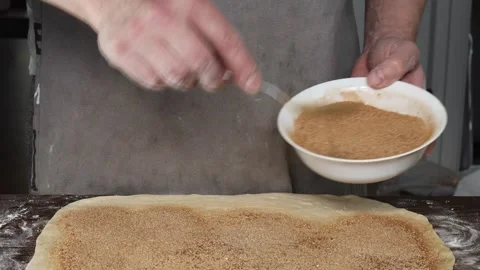 Hands sprinkling cinnamon sugar mixture onto rolled out dough during preparation Stock Footage 310337410