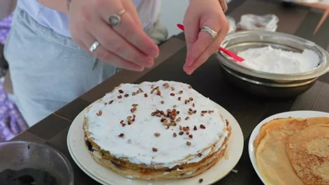 Hands Sprinkling Nuts Over Crepe Cake Layered With Whipped Cream On Table. high Stock Footage 321517143