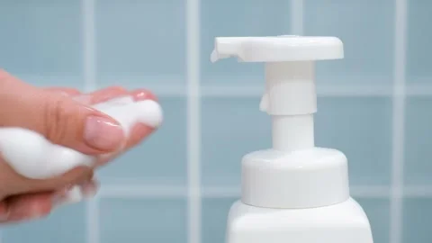 Hands squeeze liquid soap with foam from white bottle on blue tile background. Stock Footage 318871083