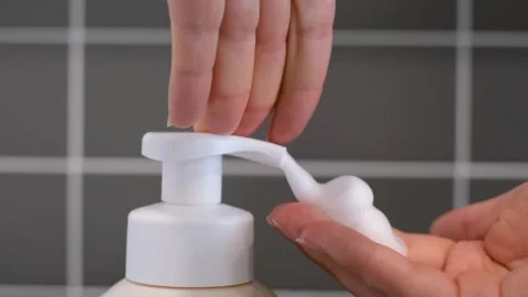 Hands squeeze liquid soap with foam from white bottle on gray tile background. 库存影片 340545006