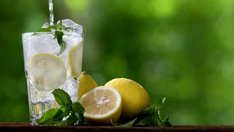 Hands squeeze out lemon juice from a slice into a glass with lemon water. Stock-Footage 336588968